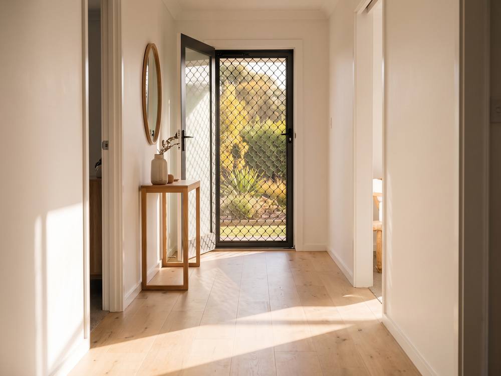 Hallway looking through an open rear security screen door to a sunlit garden