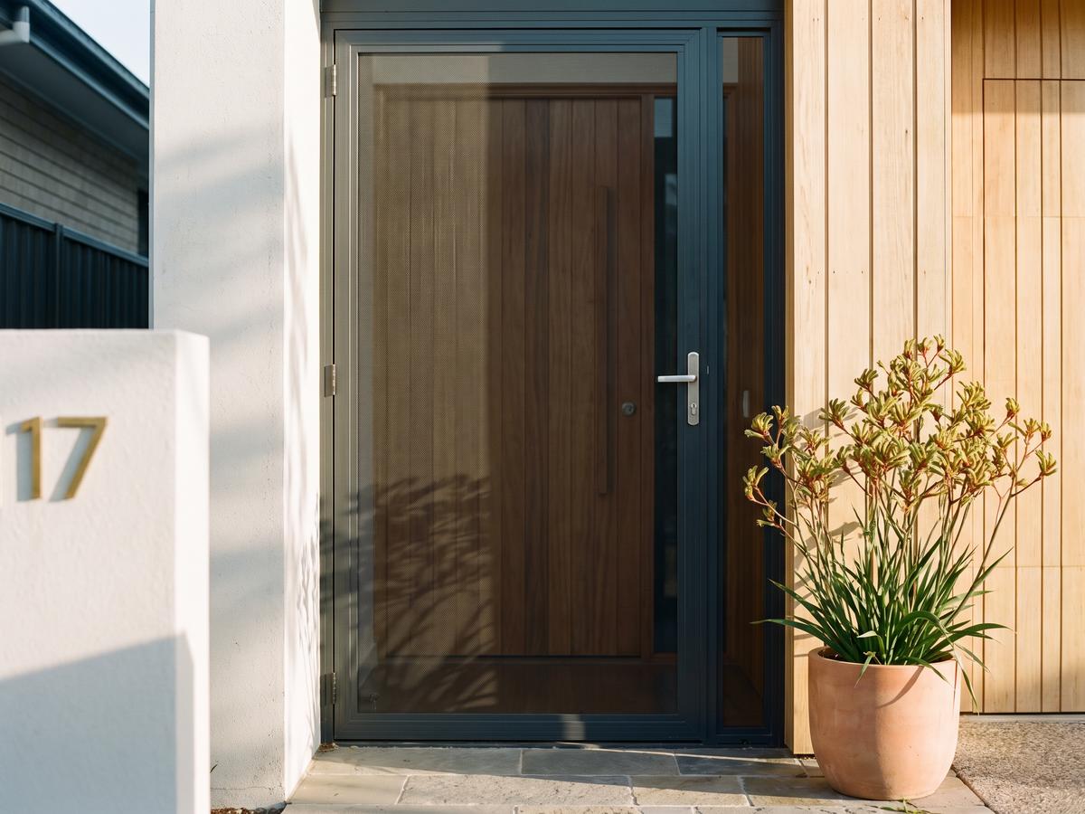 Hinged security screen door in a charcoal frame over a timber front door